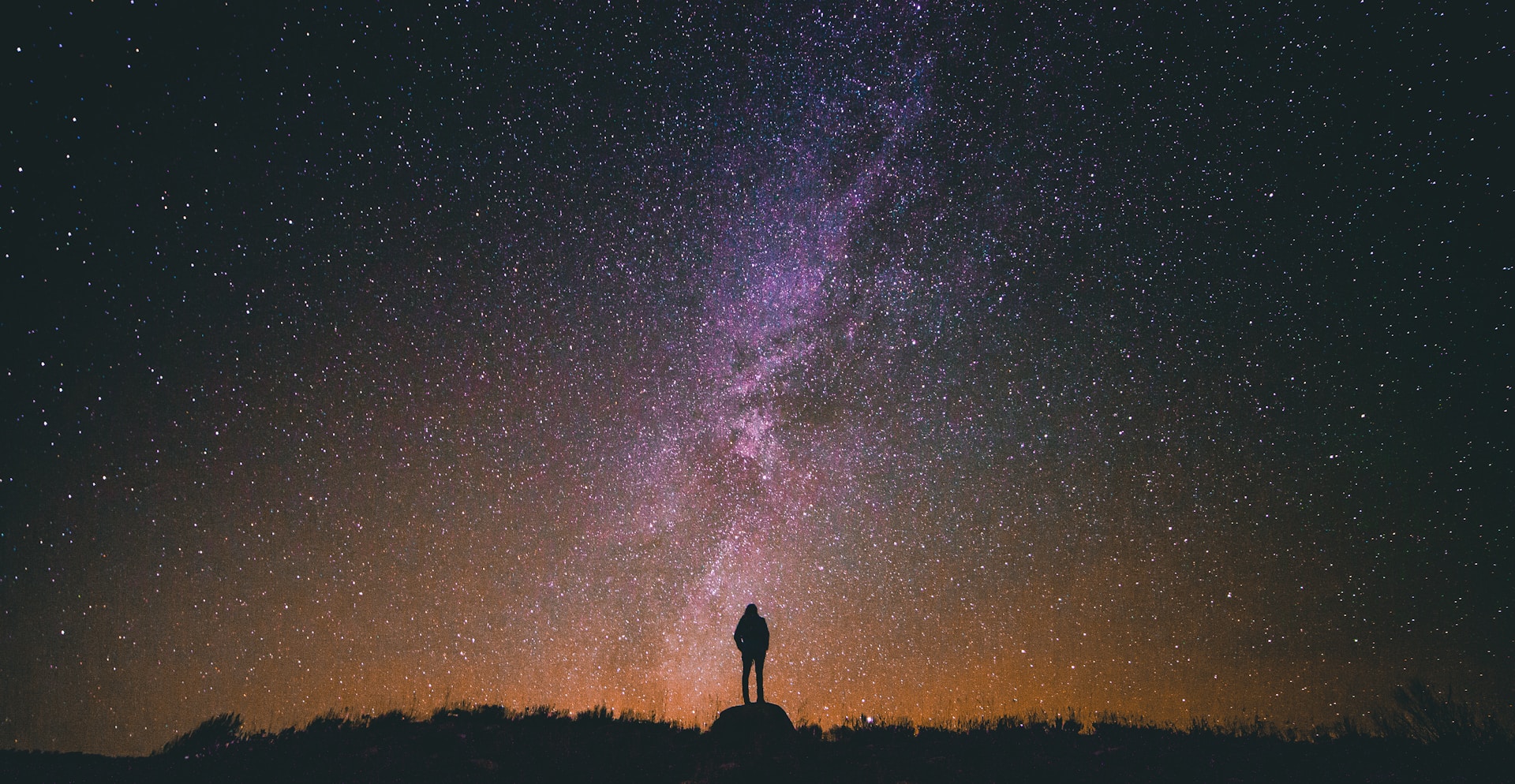Silhouette of a man standing on a rock while looking up at the sky.